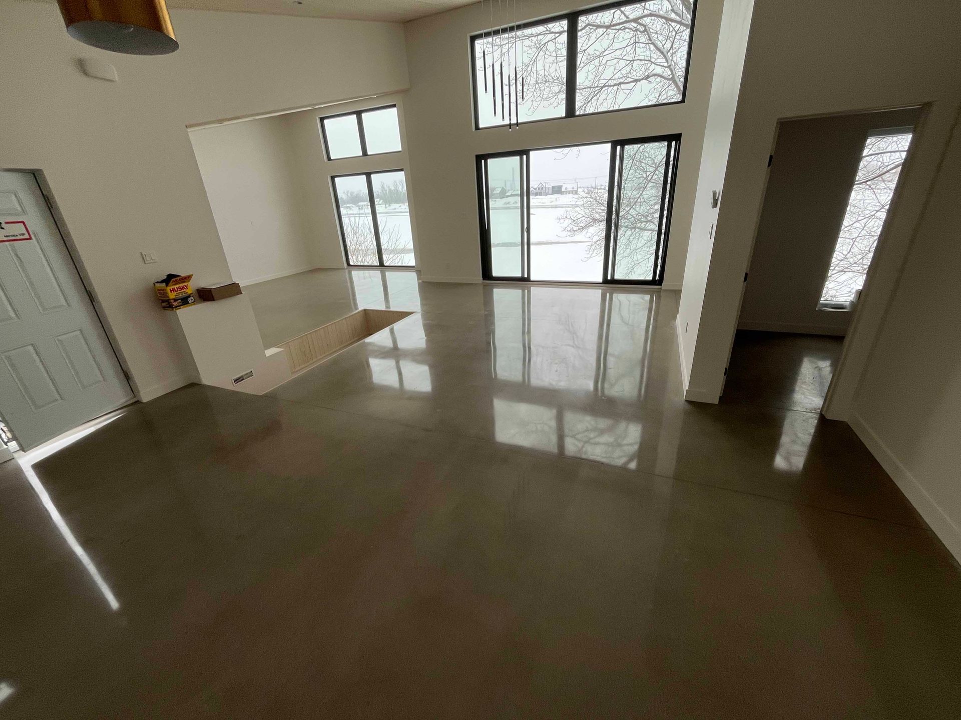 Chambre moderne vide avec sol en béton poli, grandes fenêtres donnant sur la neige.