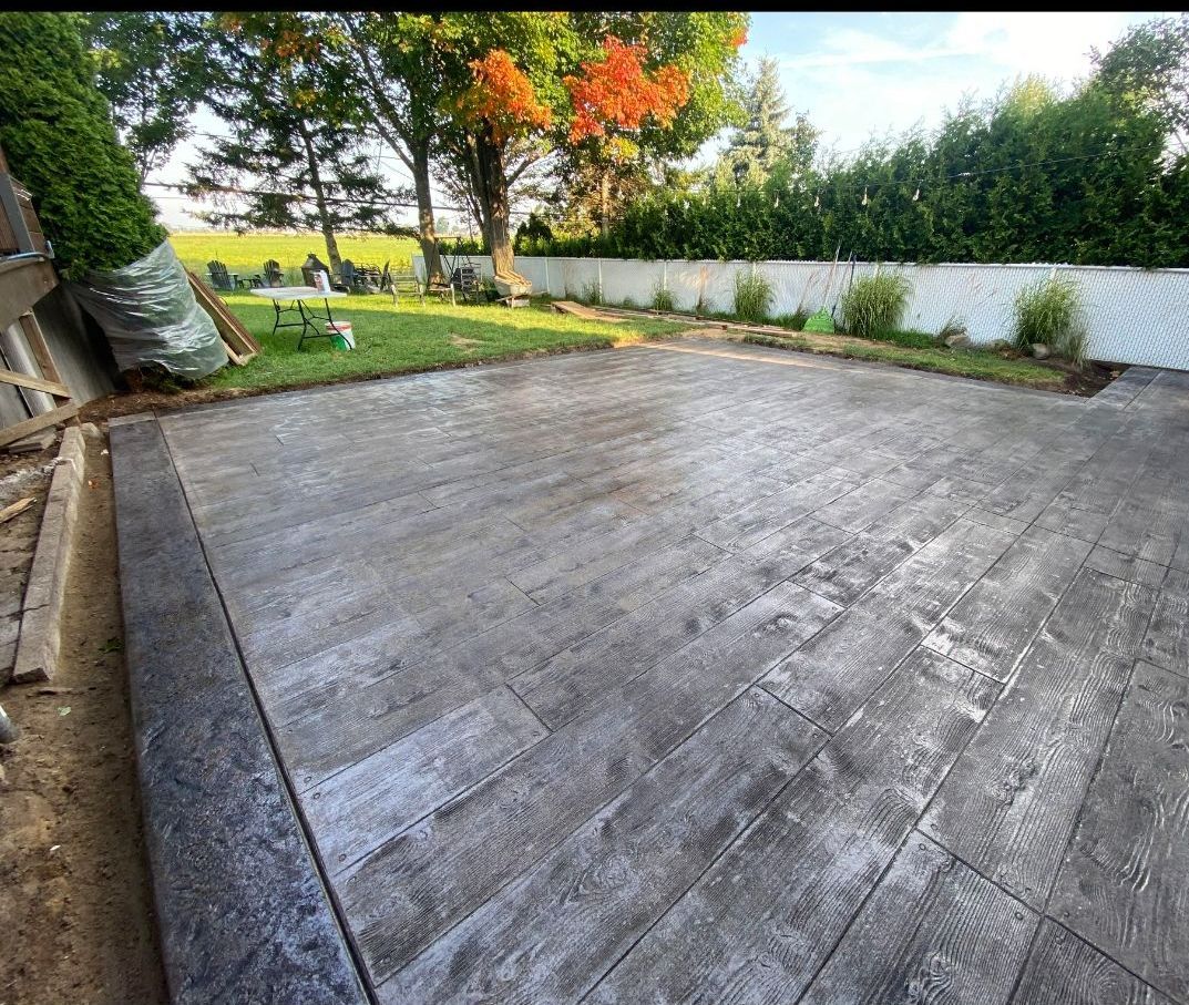 A concrete patio in a backyard with trees in the background.