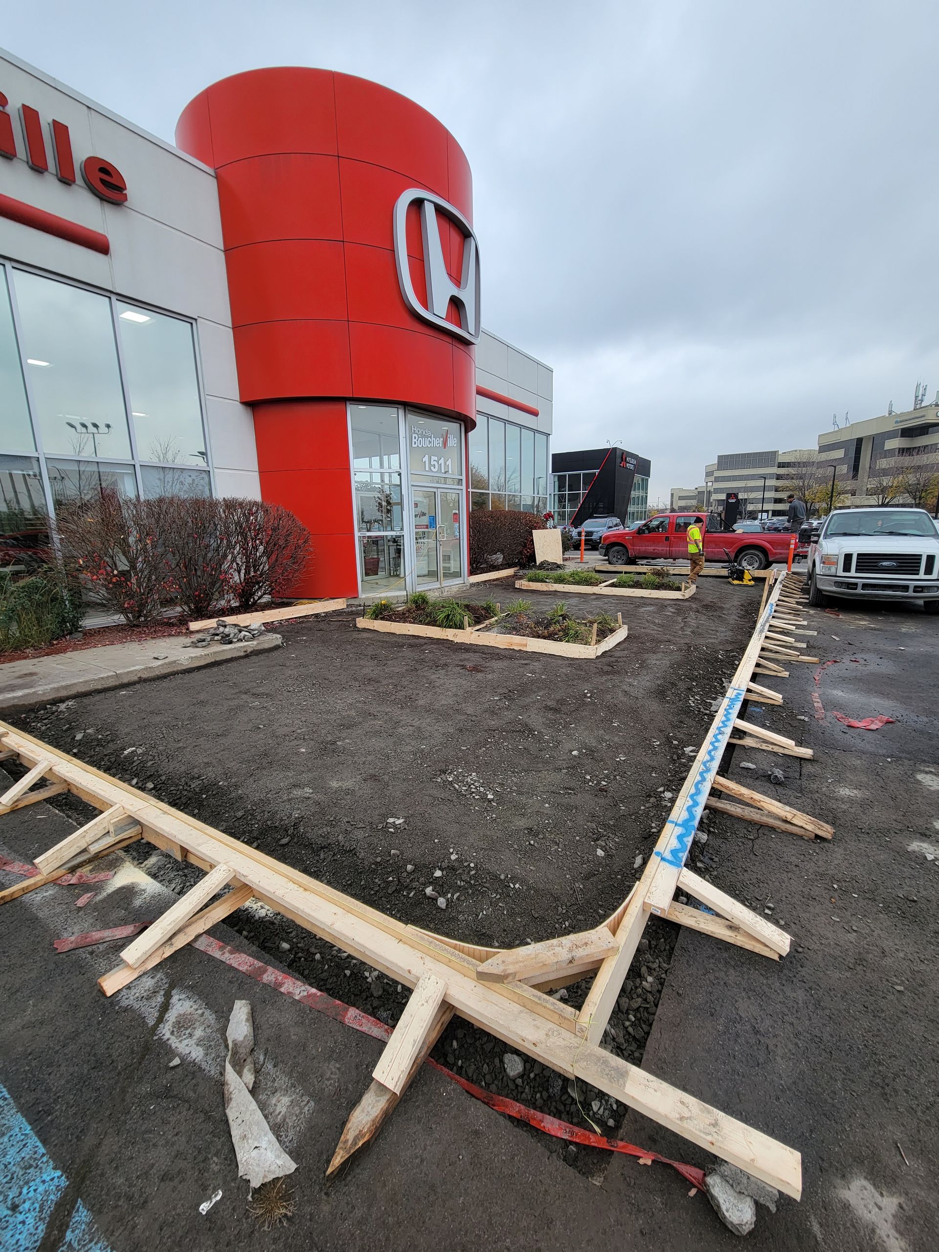 Chantier chez un concessionnaire Honda. Coffrages en bois délimitant un parterre de fleurs. Panneau Honda rouge.
