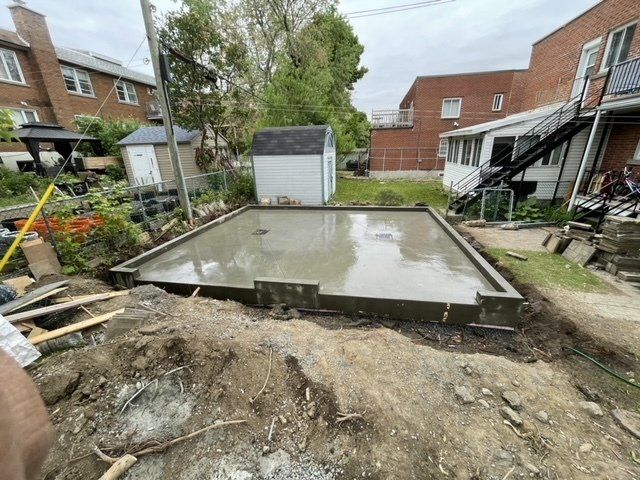 A concrete base for a house is being built in a backyard.