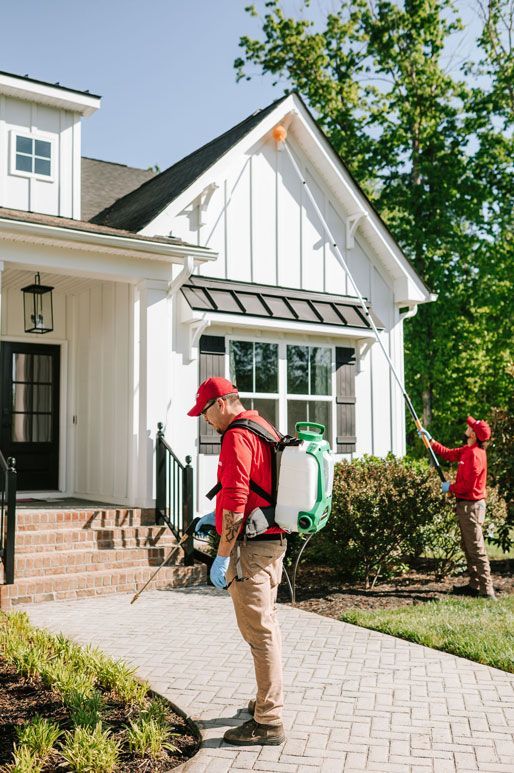 Person using a long pole to clean or inspect the upper exterior of a white house with windows.