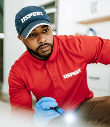 Technician in red uniform and blue gloves inspects a surface with a flashlight.