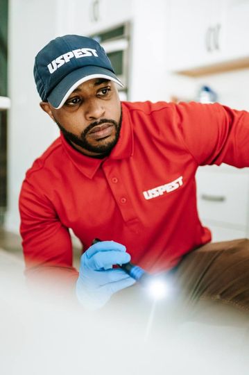 Technician in red uniform and blue gloves inspects a surface with a flashlight.