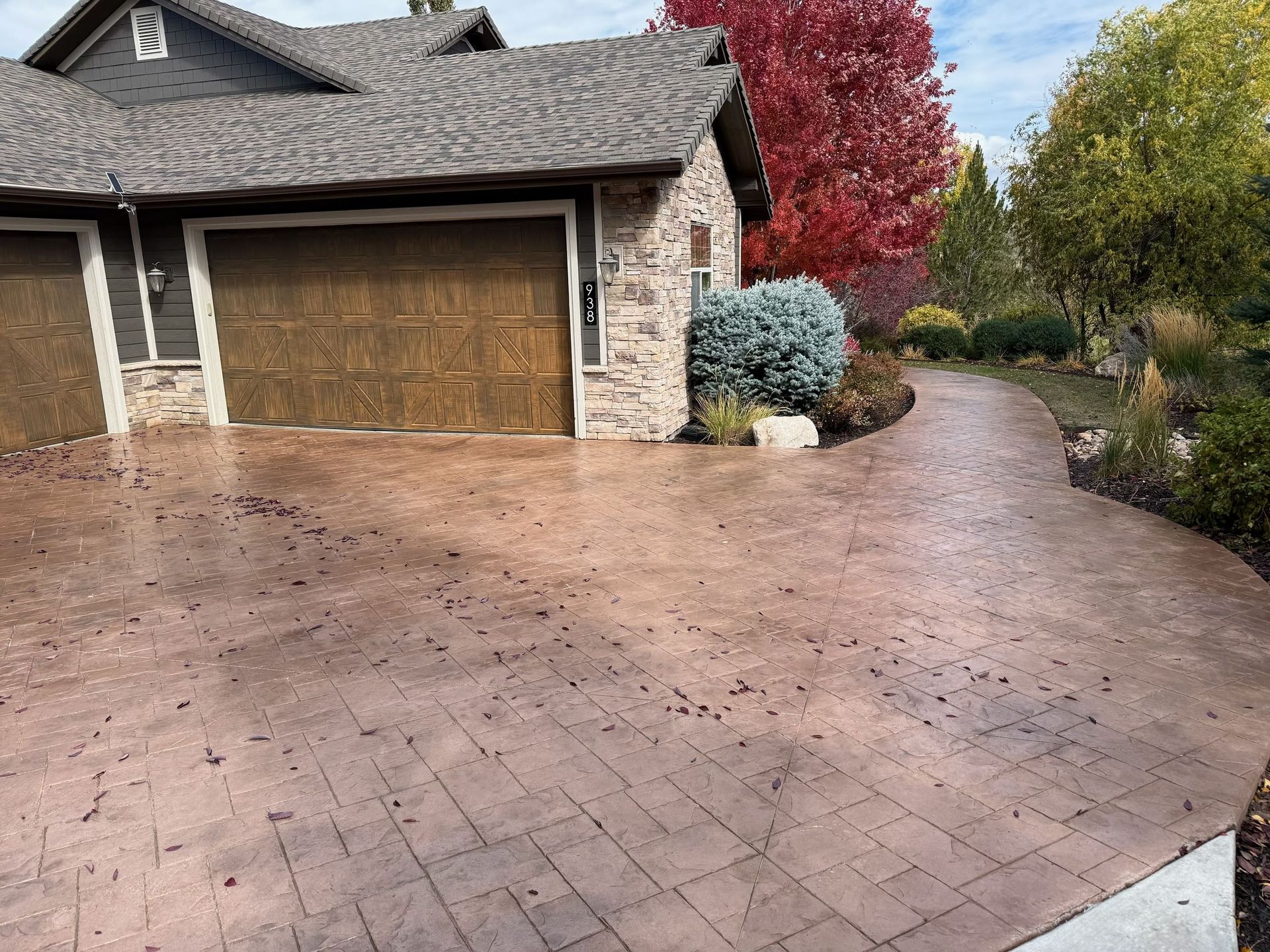 Driveway leading to a house with a brown garage door and autumn foliage.