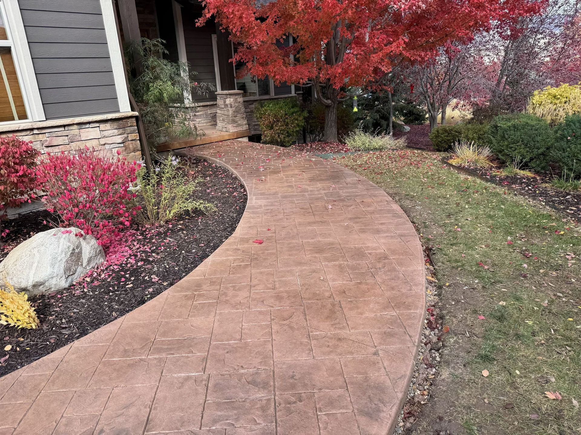Brick walkway curves toward a house with autumn foliage.