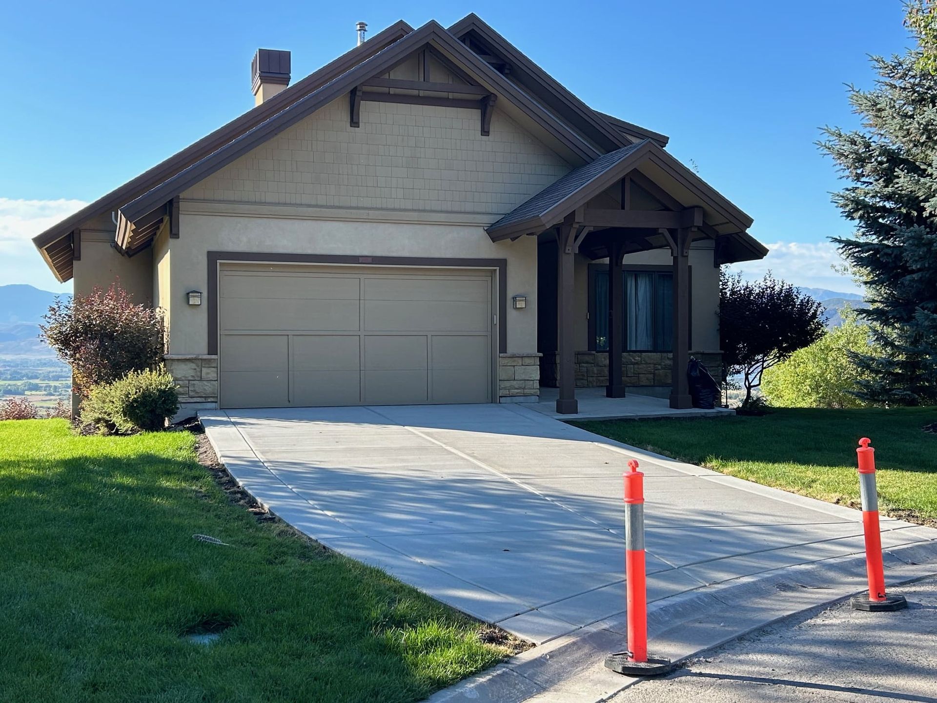 Tan house with attached garage, concrete driveway, and safety cones.