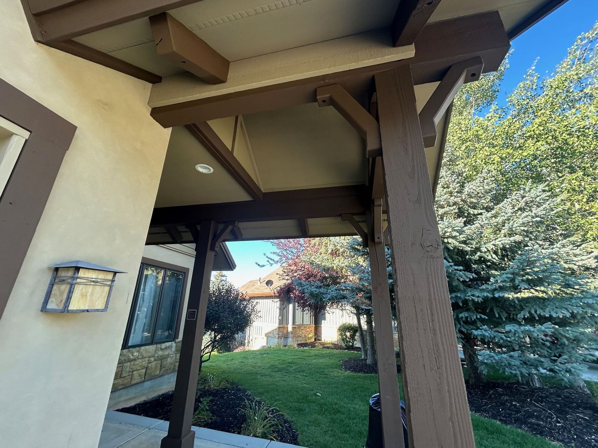 Brown-trimmed porch with a view of a house and trees on a sunny day.