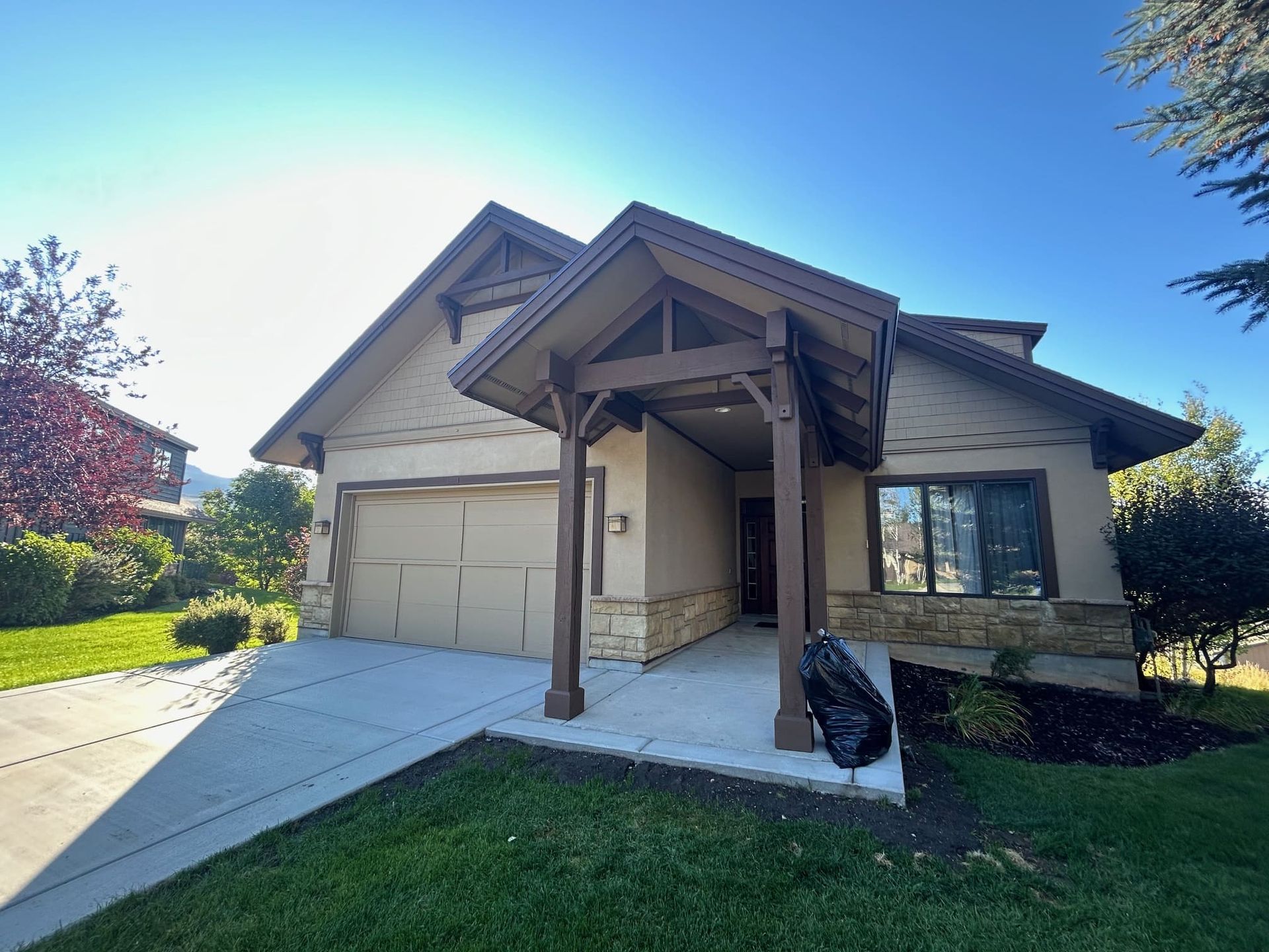 Beige house with brown trim and stone accents; concrete driveway, green lawn, clear blue sky.