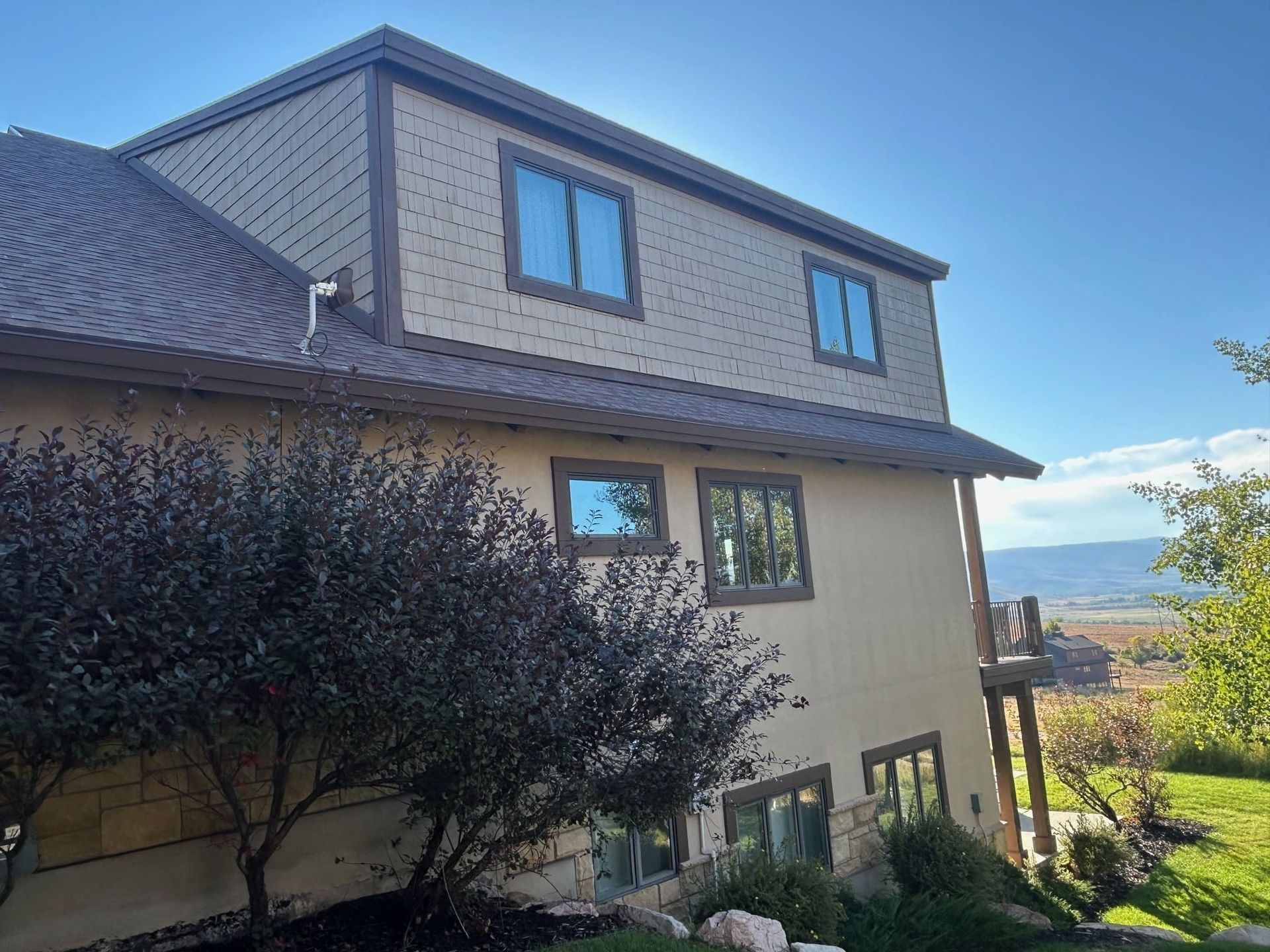 Tan house with brown trim and windows, with a shrub and blue sky background.