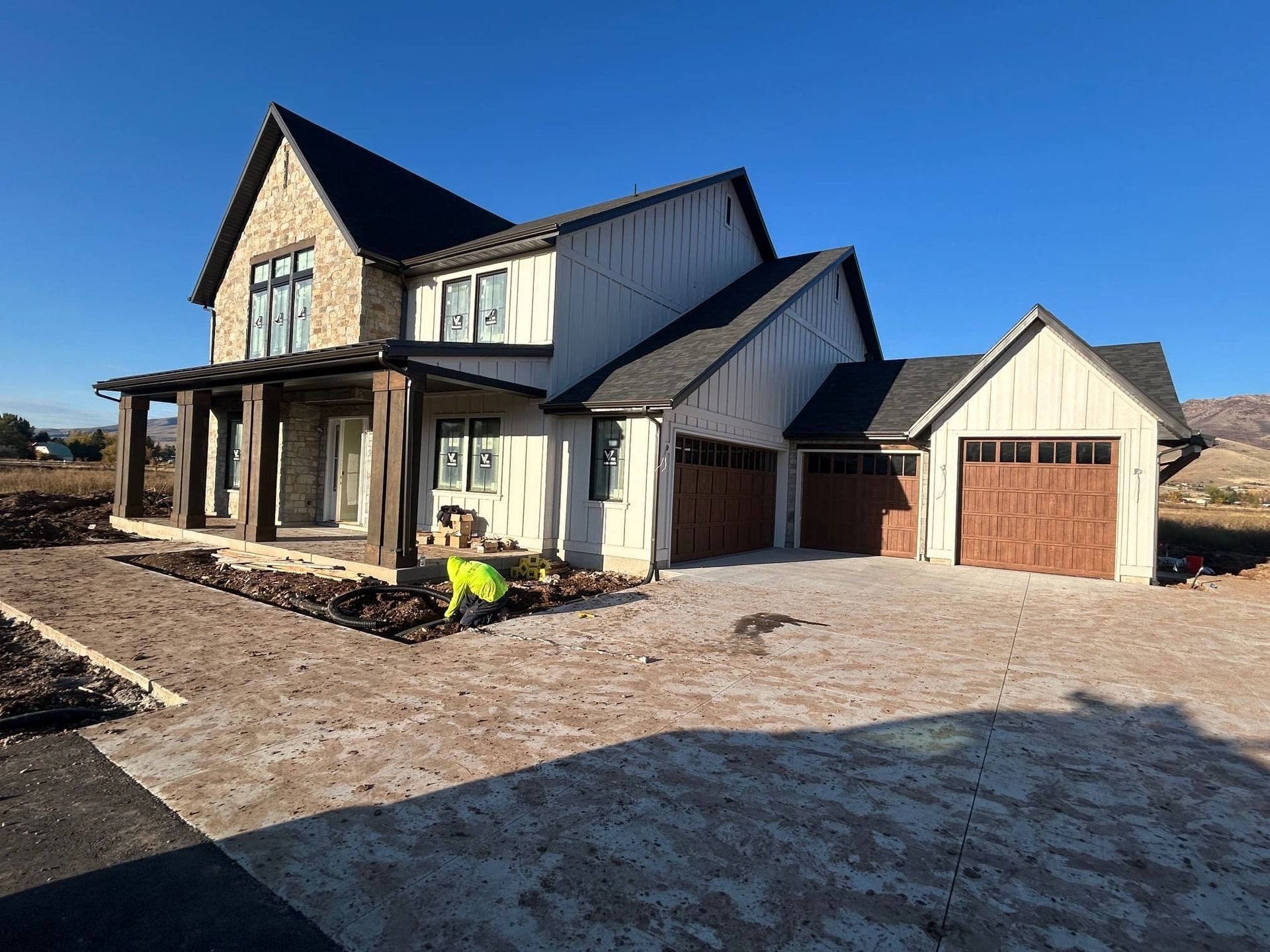 Two-story house under construction with stone and white siding, attached garage, clear blue sky.