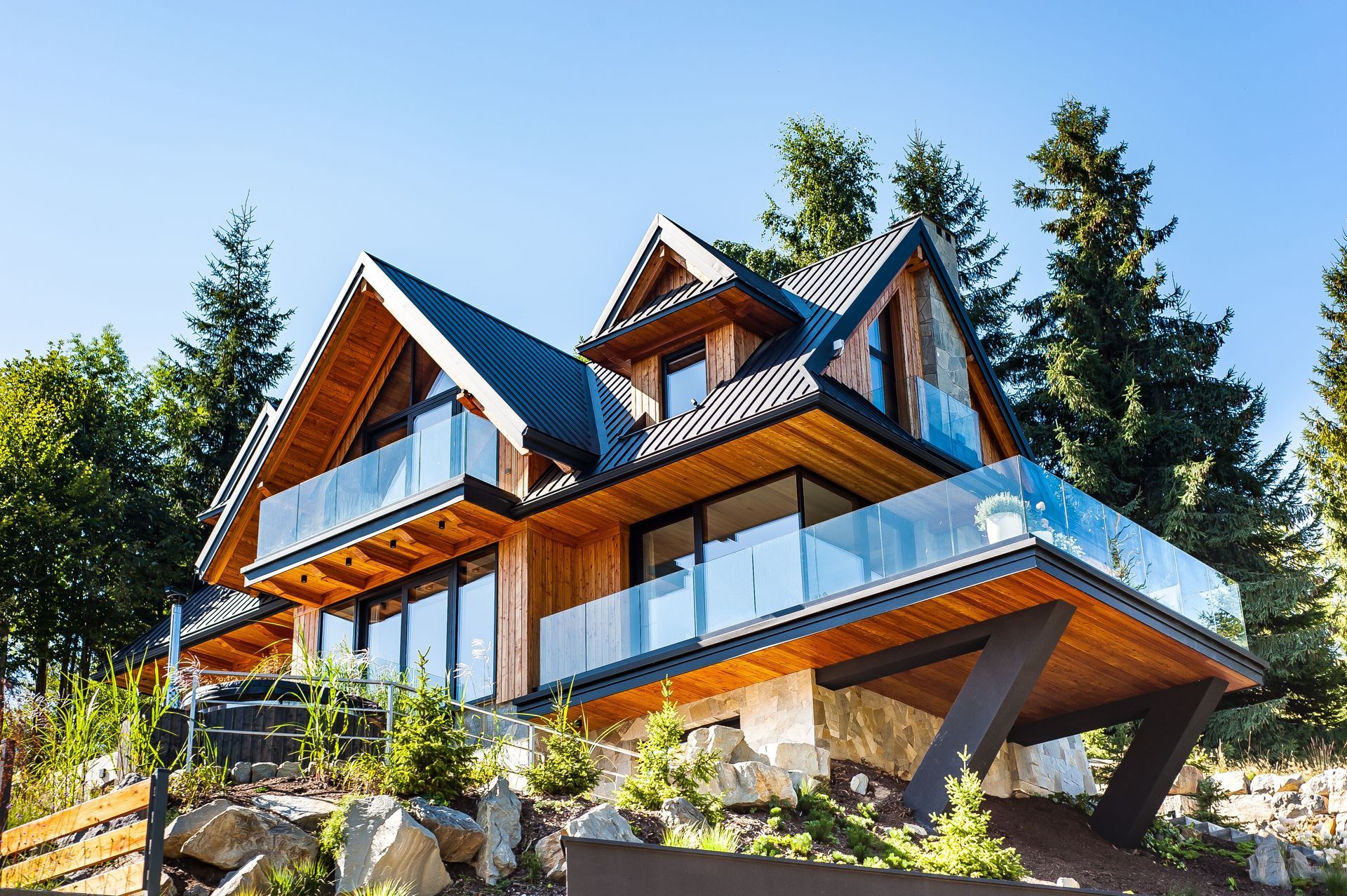 Wooden mountain home with glass balconies, against a blue sky and trees.
