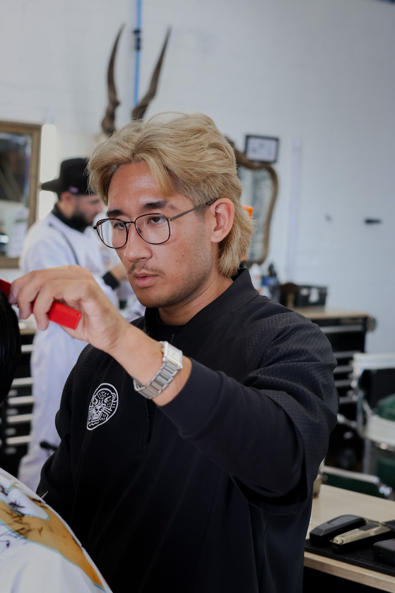 A person with blonde hair and glasses wearing a black shirt works in a hair salon.