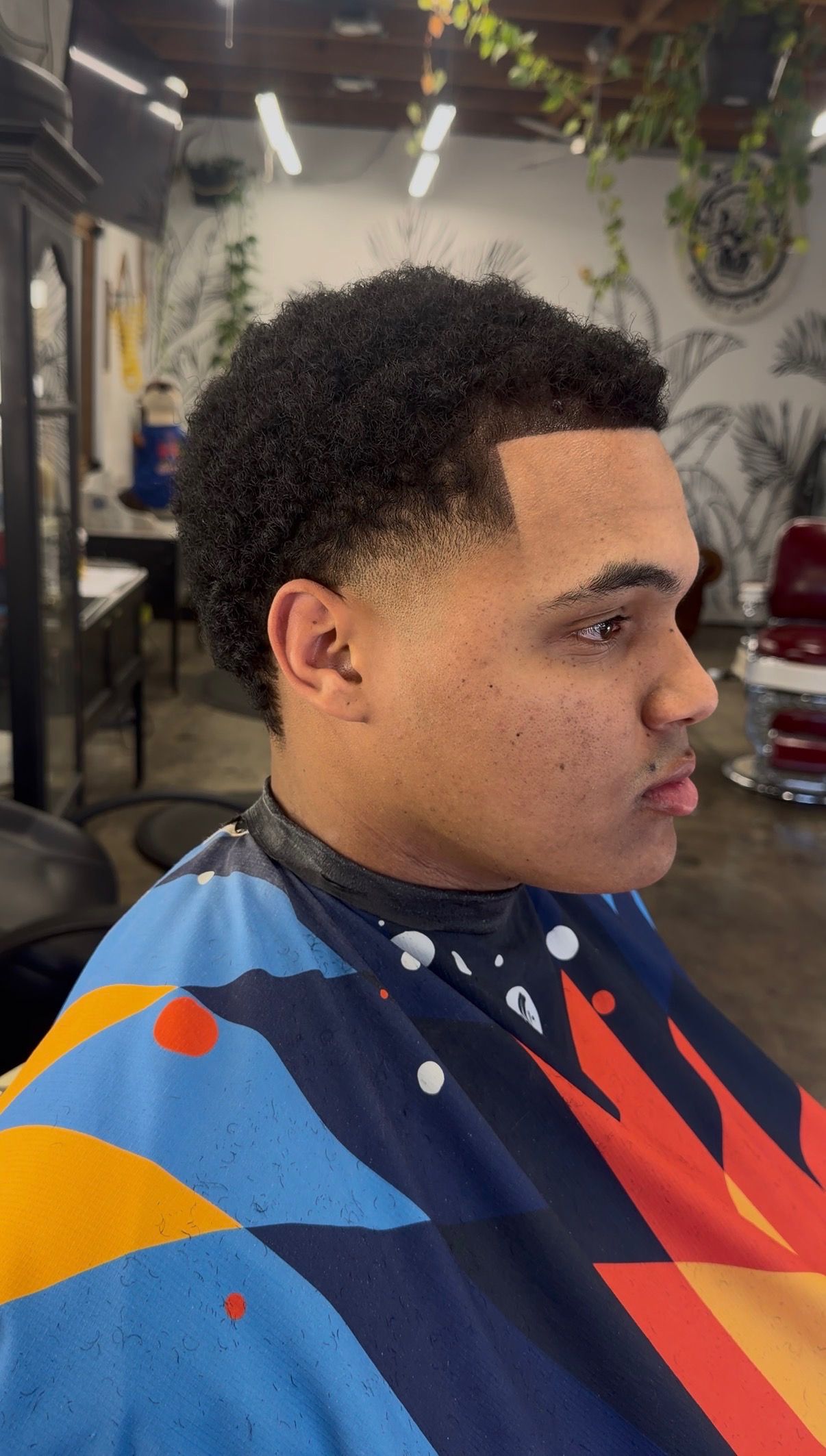 A person sitting in a salon chair, showing a fresh short haircut with a faded back and sides, inside a barbershop.