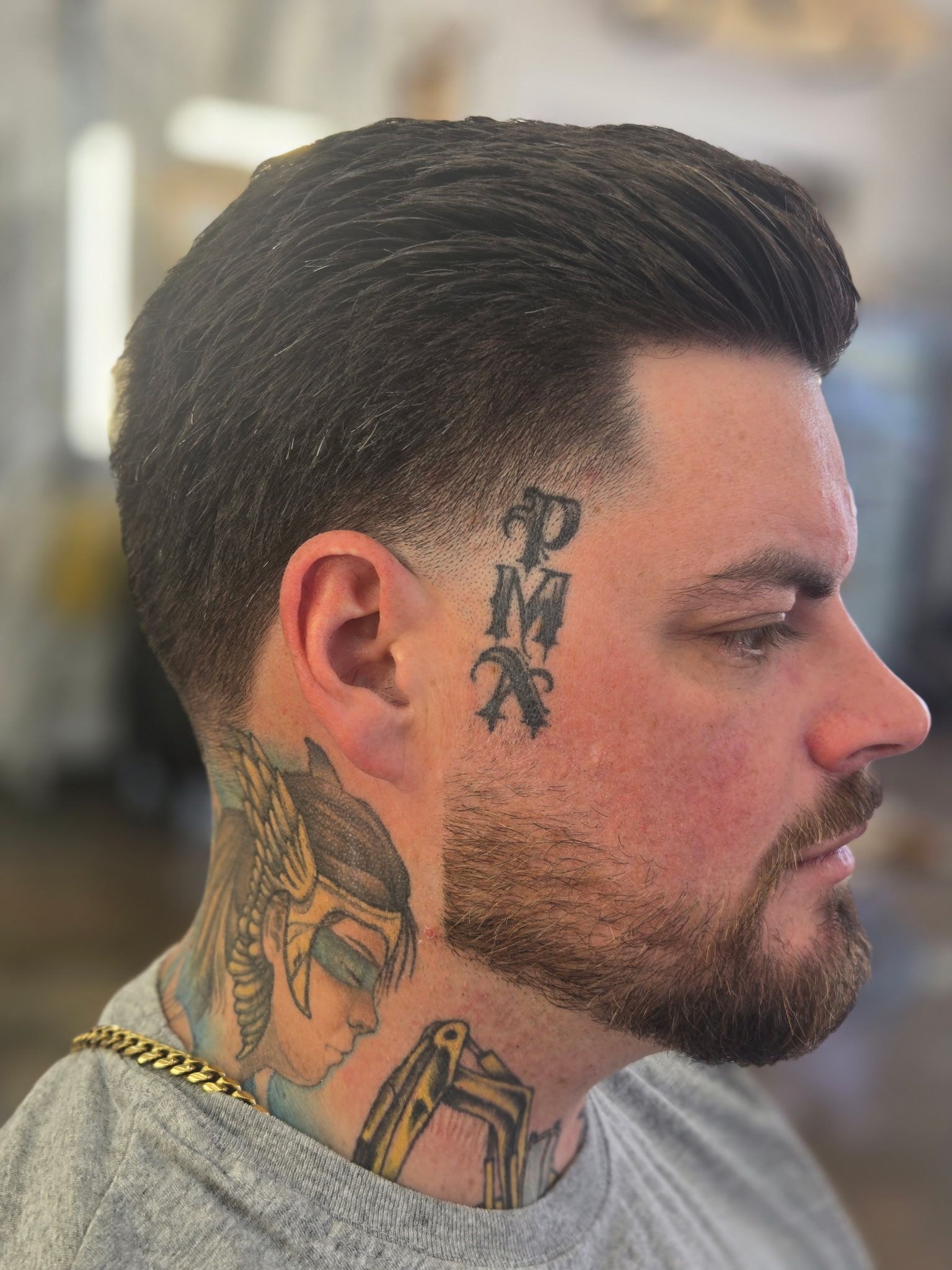 A profile view of a man with a short, faded haircut, a beard, and visible tattoos on his face and neck.