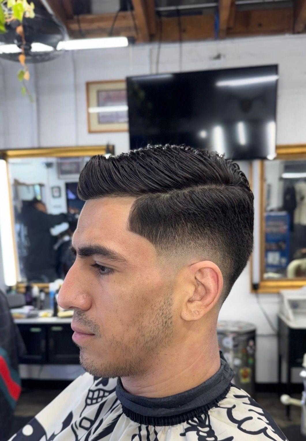 Side profile of a person in a barbershop showing a clean fade haircut with a styled, textured top.