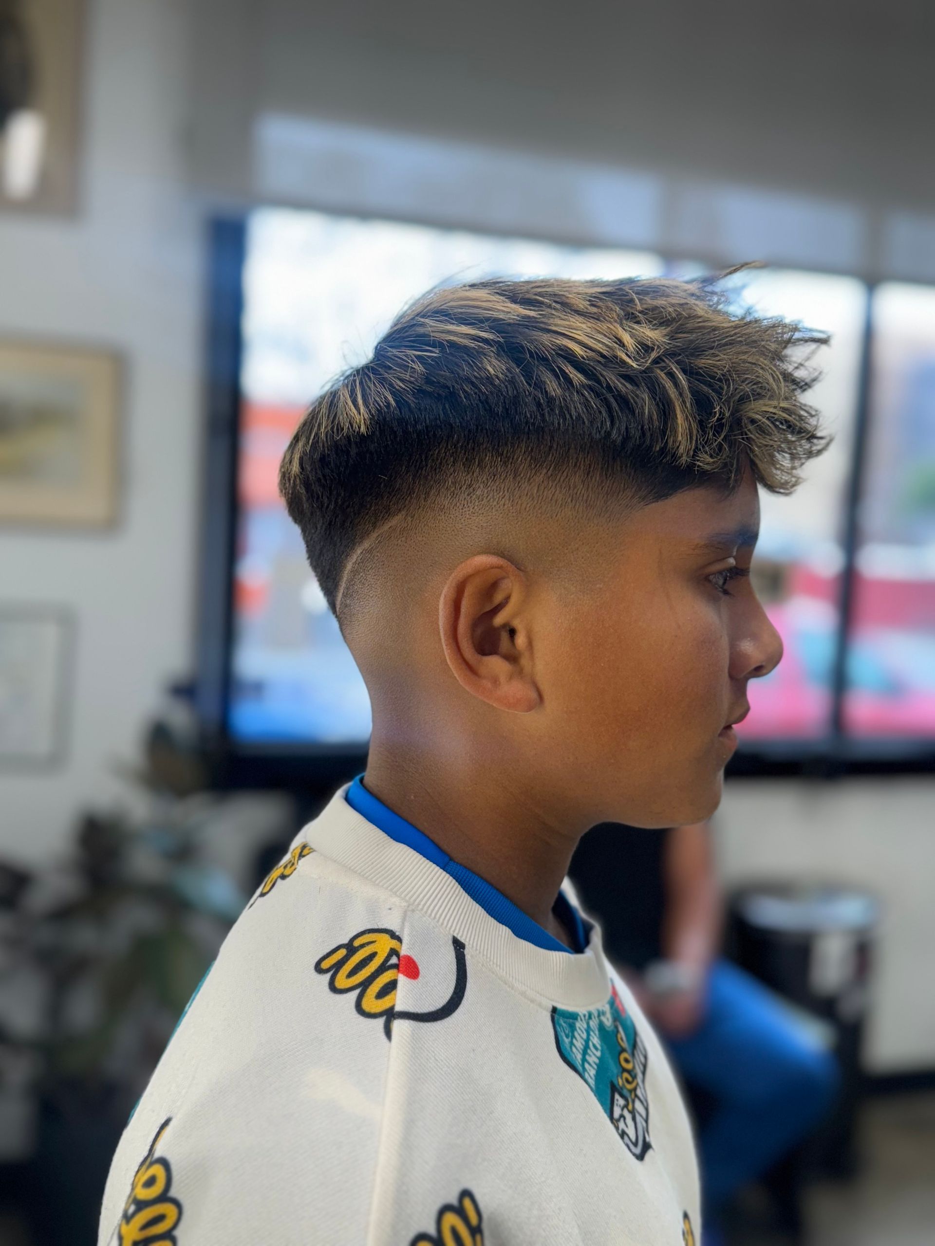 Side profile of a person with a textured, highlighted fringe and a clean skin fade haircut in a barbershop.