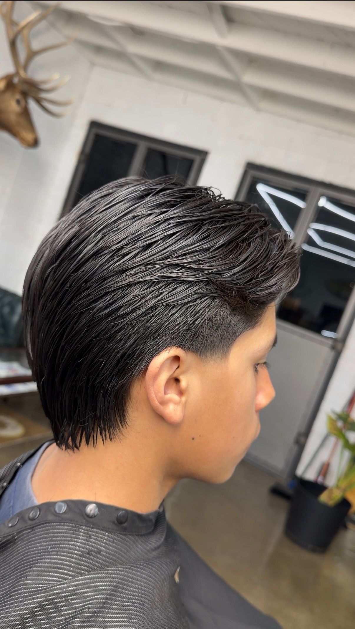 A side view of a person’s textured, dark hair styled in a modern cut with faded sides, set in a bright room.