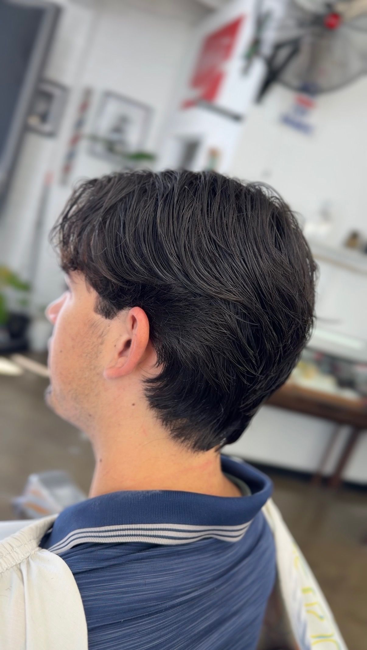 A side profile of a person in a salon chair with dark, medium-length wavy hair featuring a textured, layered cut.