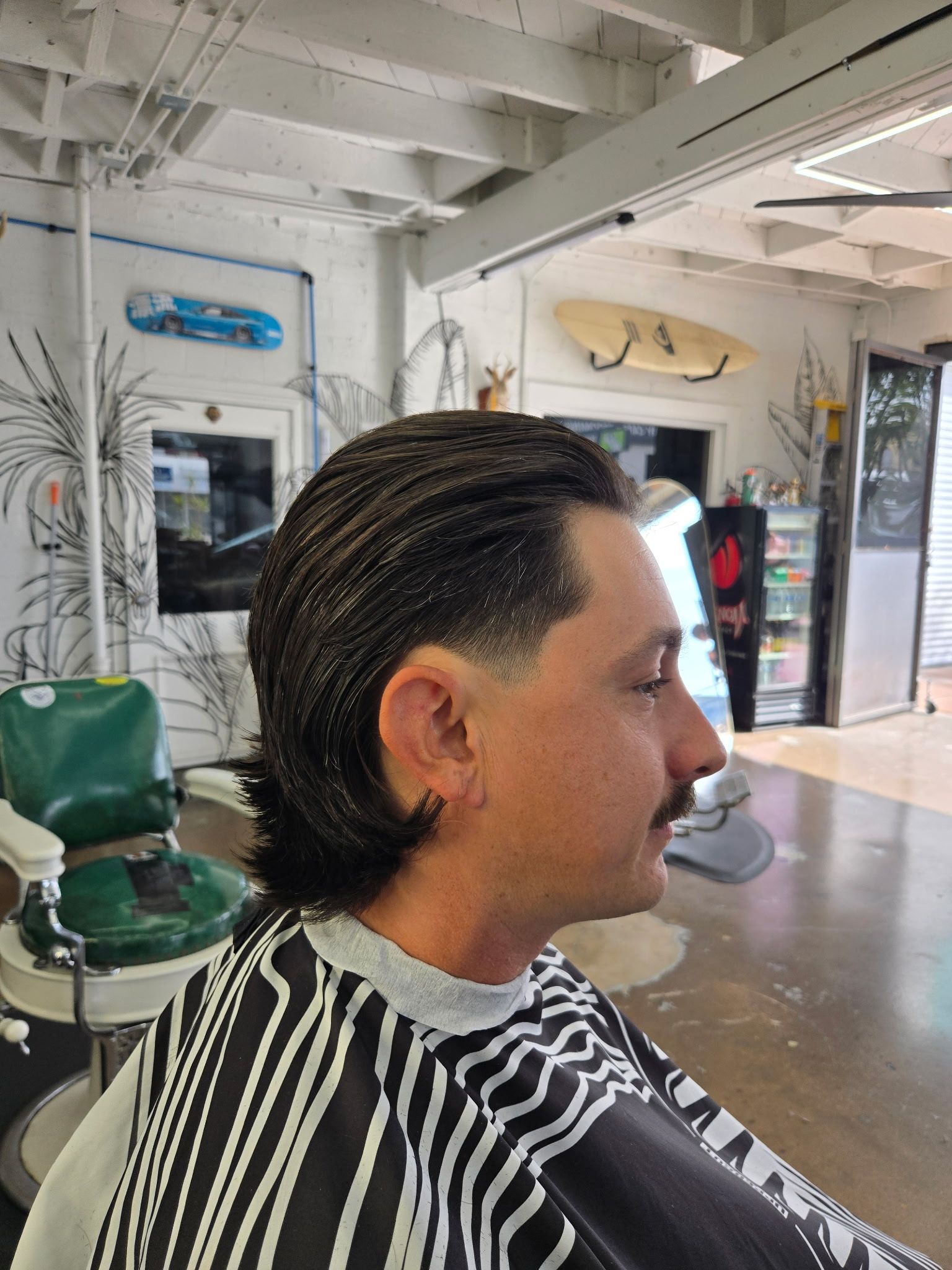 Side profile of a person with a slicked-back haircut and a faded temple in a barbershop.