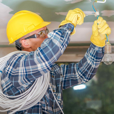 Electrician in yellow hard hat and gloves, installing light fixture.