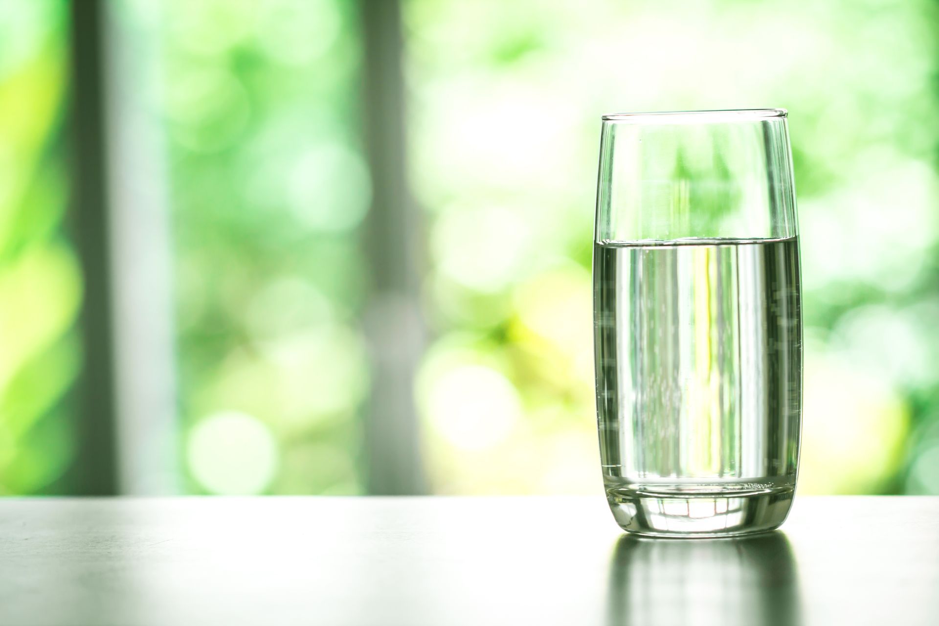 A glass of water is sitting on a table in front of a window.