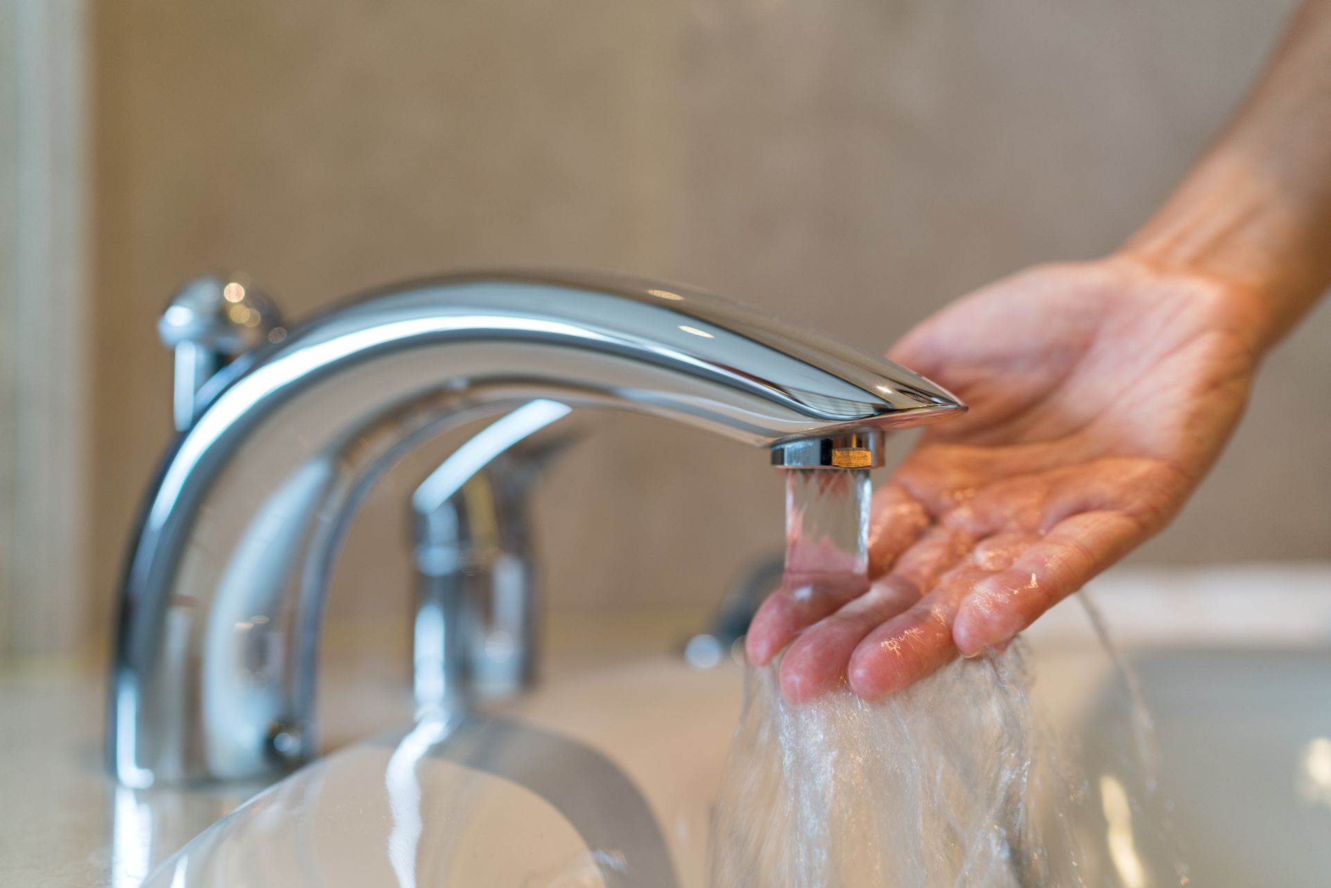 A person is washing their hands under a faucet in a bathroom.