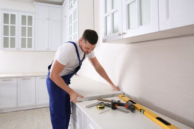 Worker measuring countertop in a bright white kitchen with tools on the counter