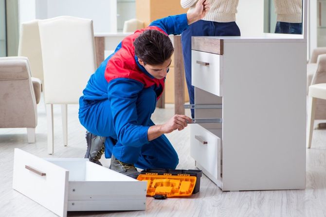 Person in blue overalls repairing a white dresser with orange tool kit on the floor