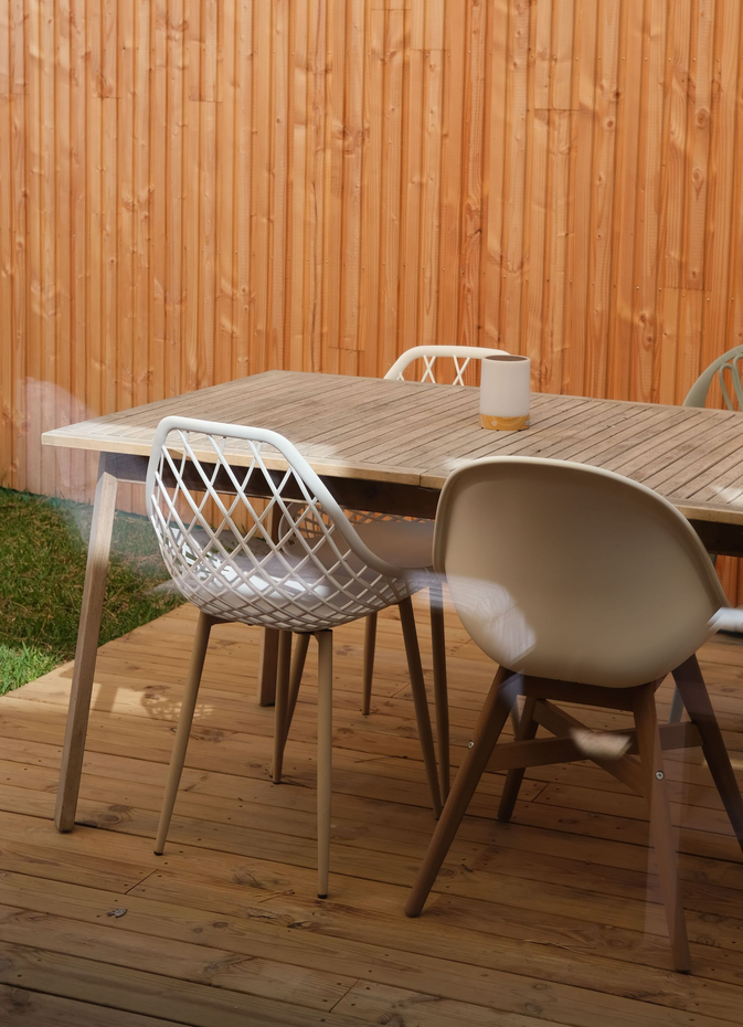 Outdoor dining table with woven chairs against a bamboo fence and wooden deck.