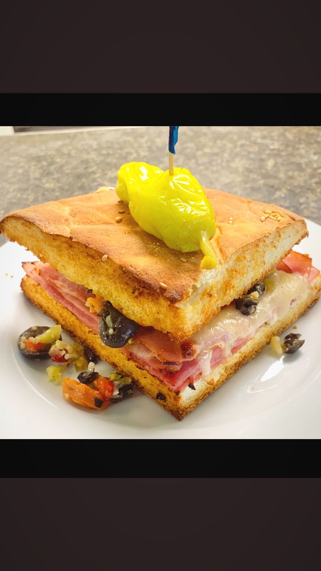 Cuban sandwich on white plate, garnished with olives and pepperoncini.