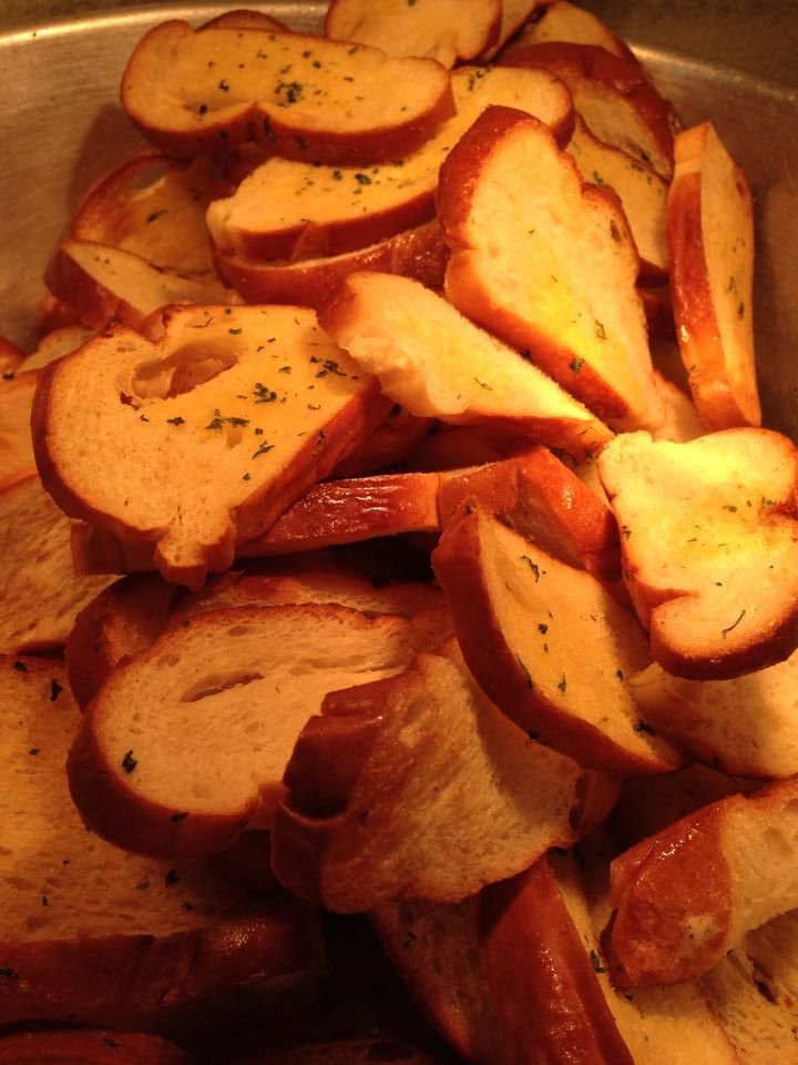 Garlic bread slices, golden-brown and herb-sprinkled, piled in a metal container.