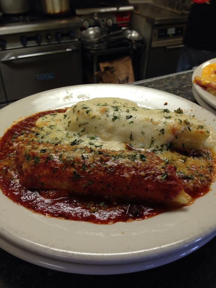 Enchilada covered in red sauce and cheese, on a white plate, in a restaurant.