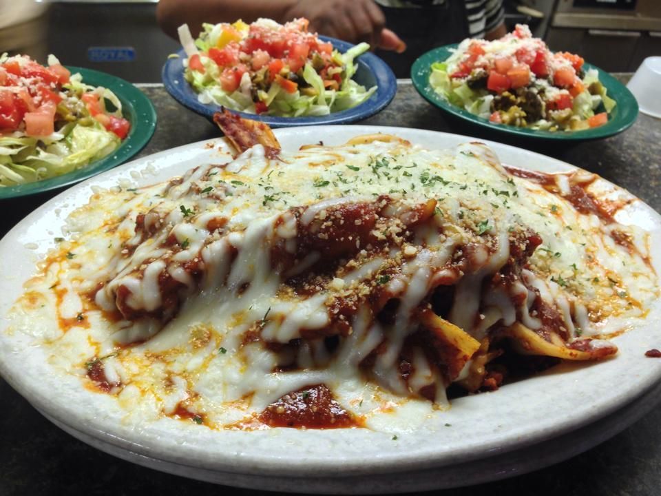 Pasta dish covered in melted cheese with salads in the background.