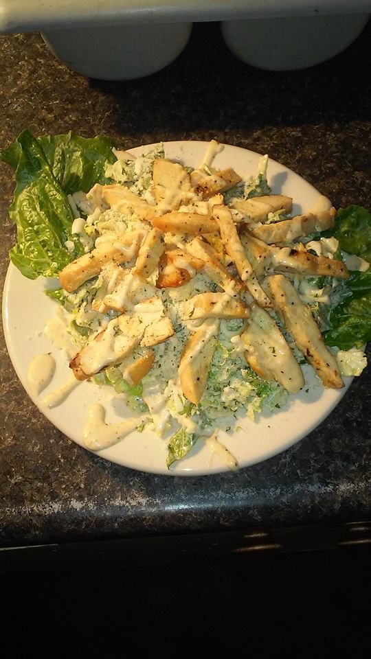 Caesar salad with grilled chicken on a white plate, dark countertop.