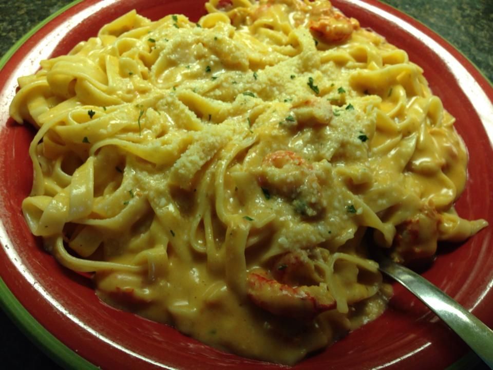 Fettuccine pasta with creamy sauce and lobster on a red plate.