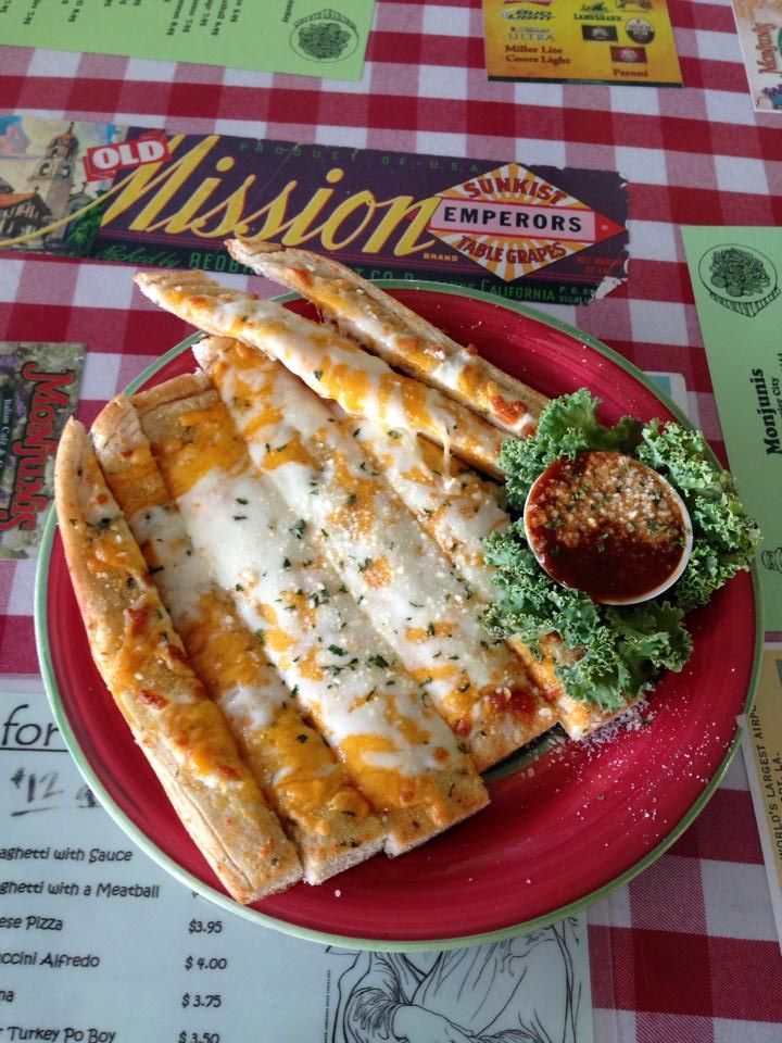 Garlic bread with cheese on a red plate, served with marinara sauce. Plaid tablecloth in the background.