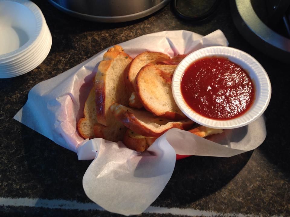 Sliced bread with dipping sauce in a basket, atop a dark surface.
