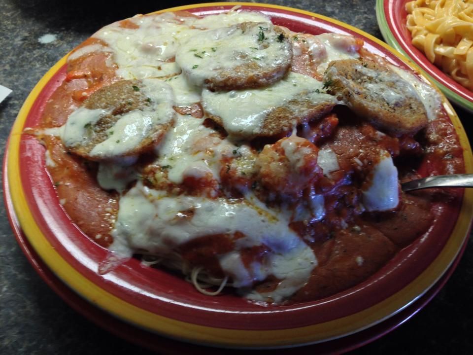Chicken parmesan on a colorful plate, covered in melted cheese and tomato sauce, with pasta in the background.