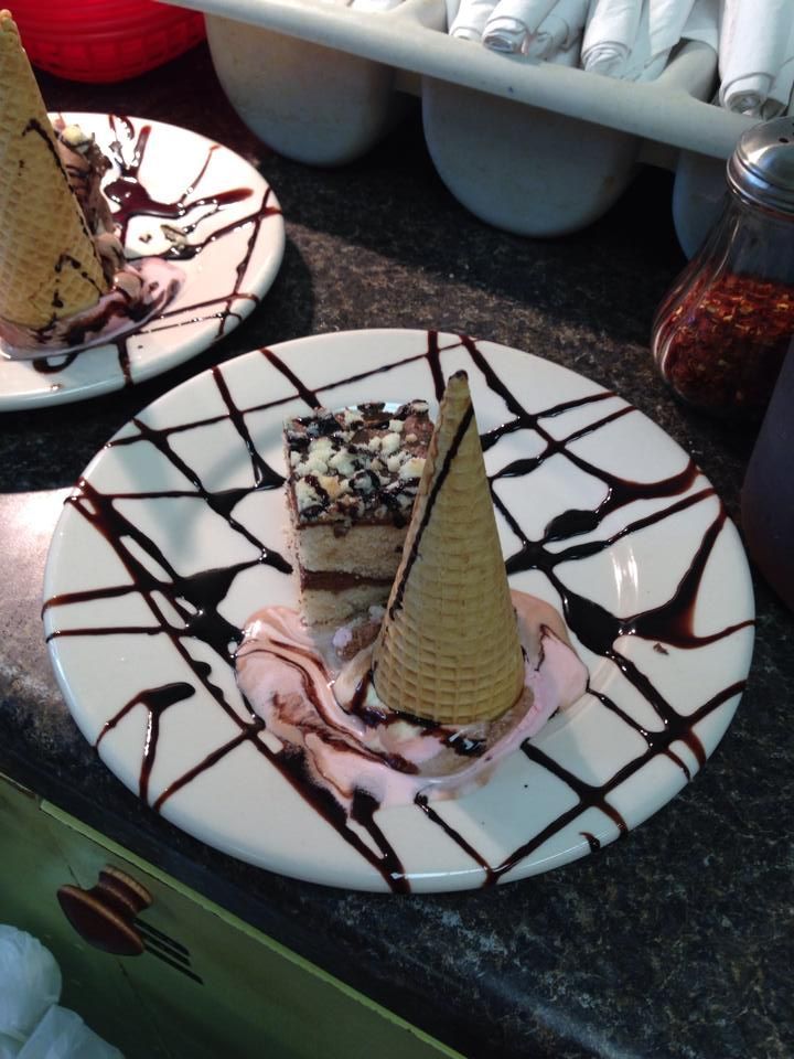Dessert plate with slice of cake, ice cream, and upside-down cone drizzled with chocolate.