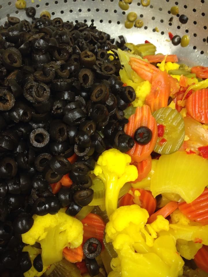 Colander filled with sliced black olives, yellow cauliflower, carrots, and pickles.