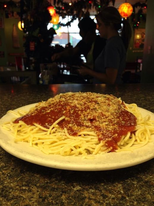 Spaghetti with red sauce and grated cheese on a white plate, with restaurant staff in the background.