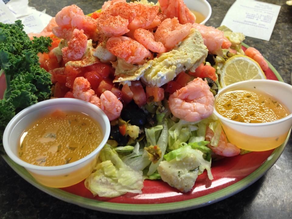 Plate with shrimp salad, tomatoes, lettuce, lemon, and two dipping sauces.