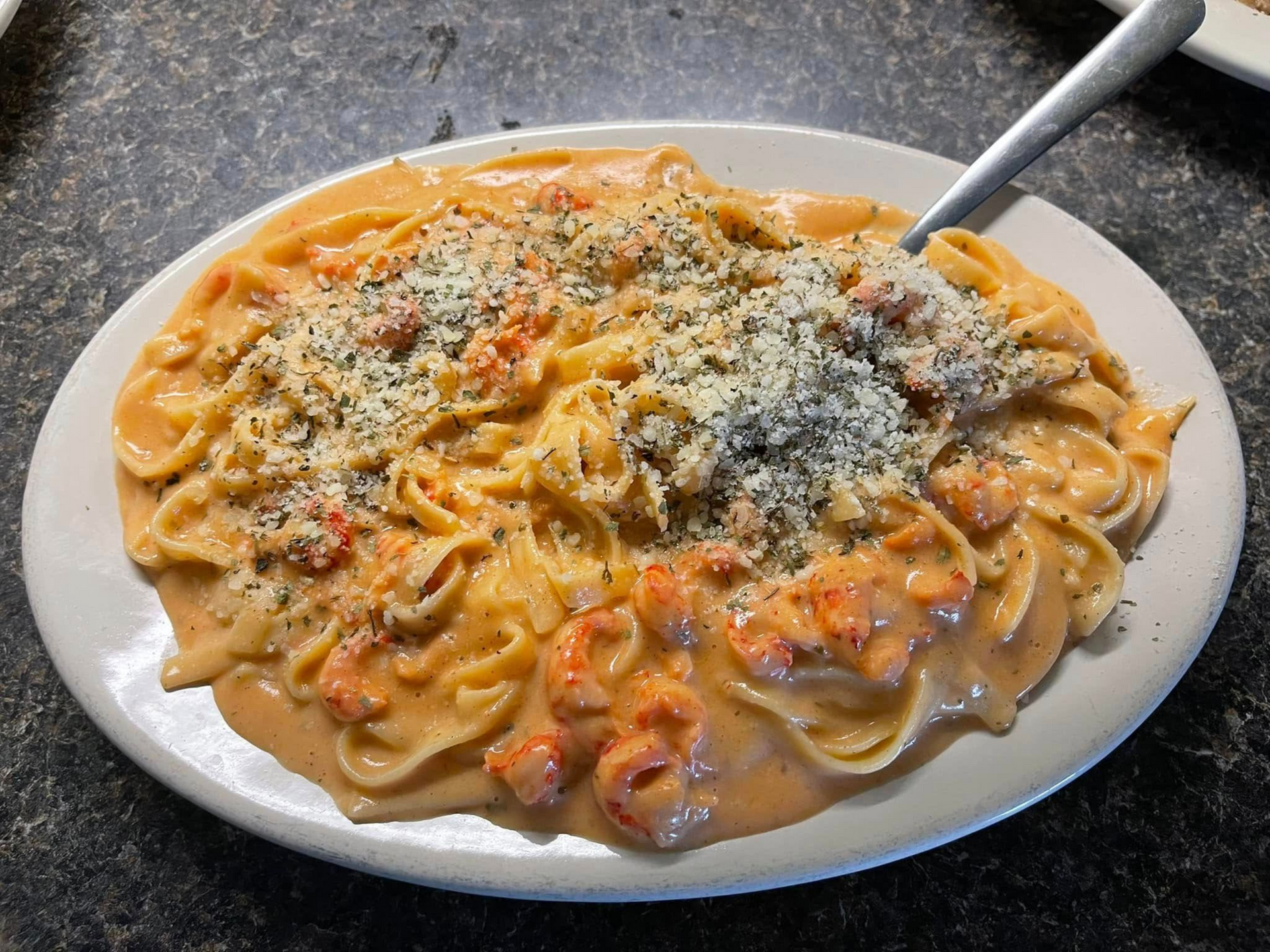Pasta with creamy sauce and crawfish, garnished with cheese and herbs on a white plate.