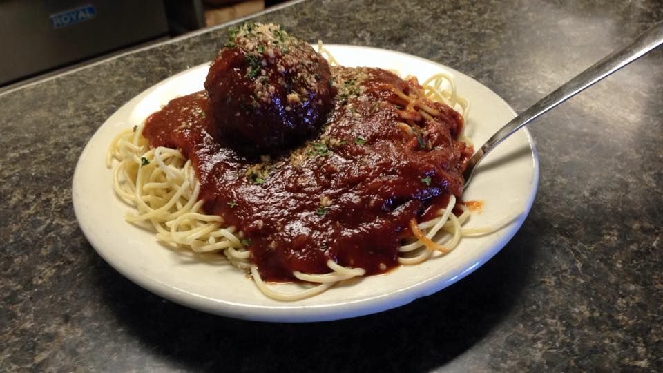 Plate of spaghetti with a large meatball, covered in red sauce, on a countertop with a fork.