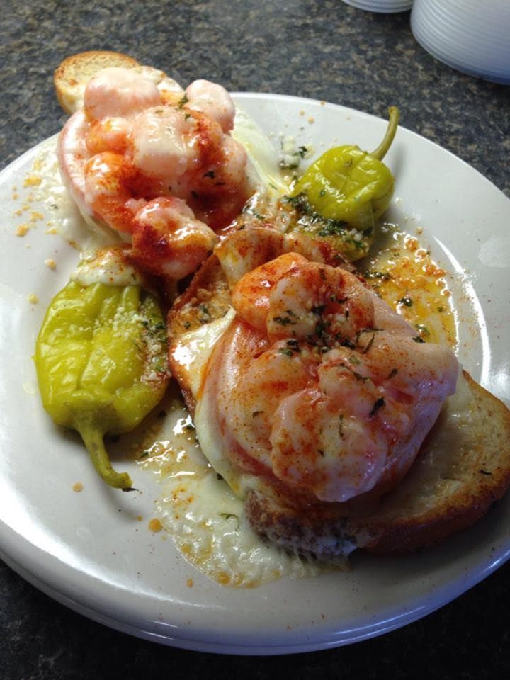 Shrimp scampi on toasted bread with pepperoncini. White plate, dark counter.