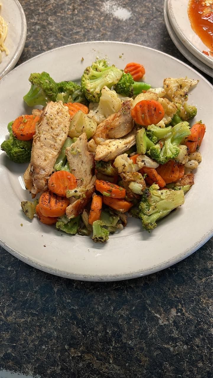 Chicken and roasted vegetables on a white plate, including broccoli, carrots, and cauliflower.