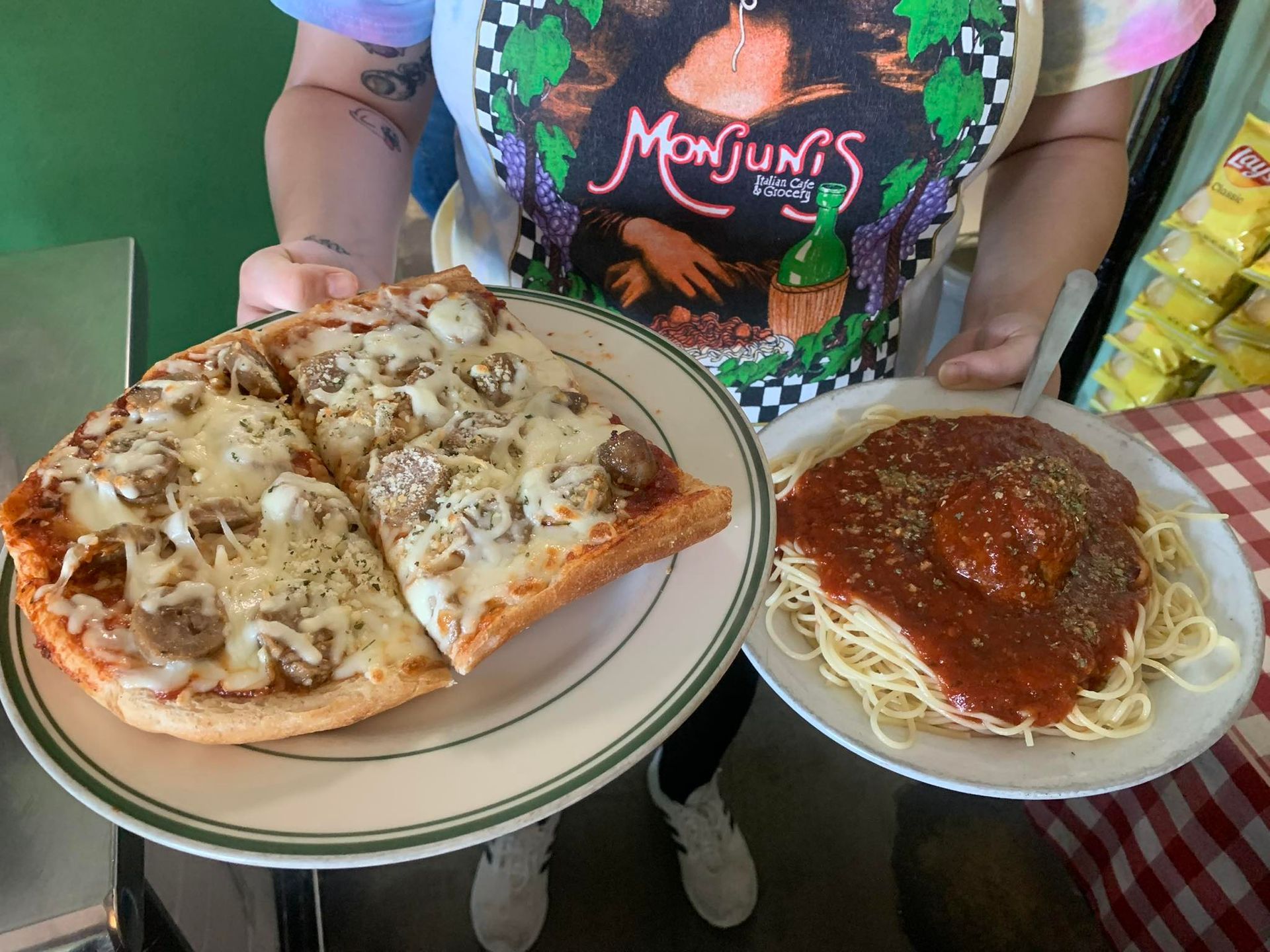 Person holding plates of pizza slices and spaghetti with meatball at a restaurant.