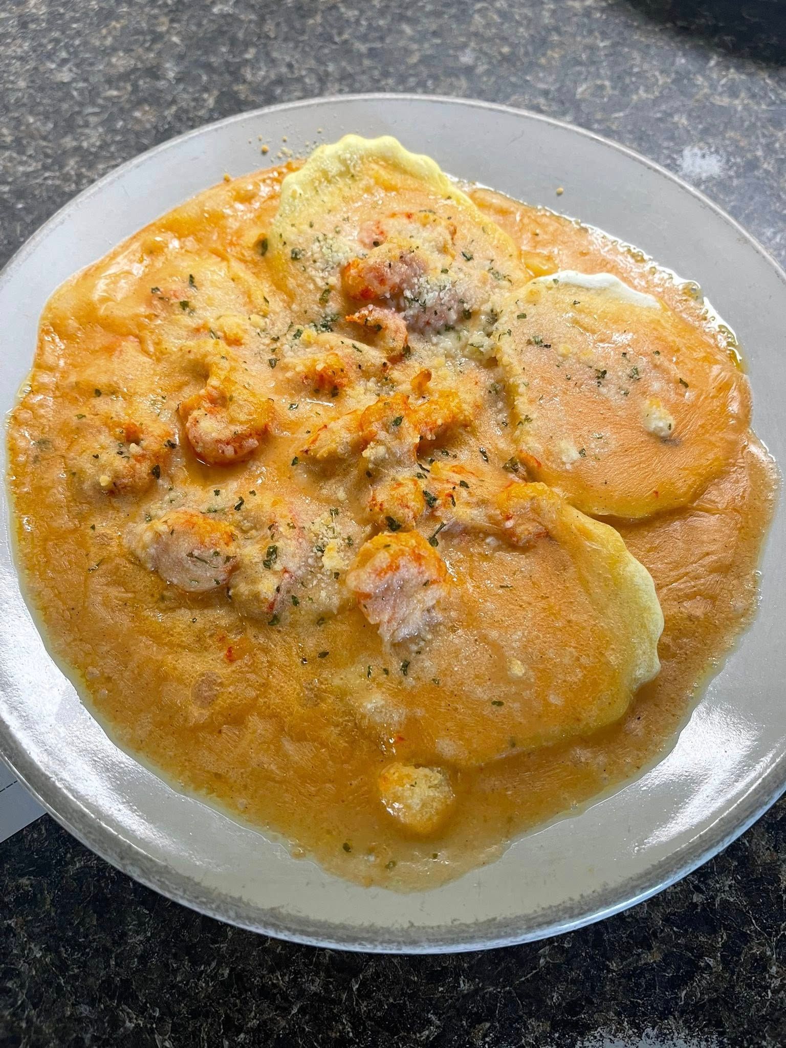 Yellow-orange cheesy grits with shrimp, served on a clear plate.
