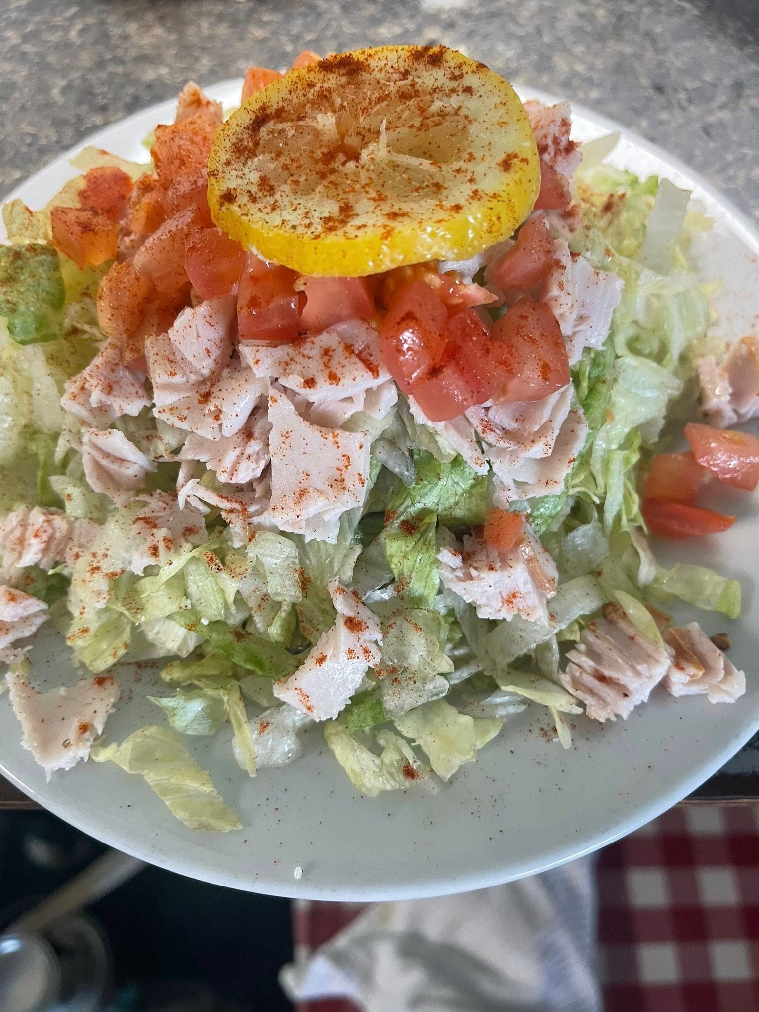 Salad with turkey, tomatoes, lemon slice, and paprika, on a white plate.