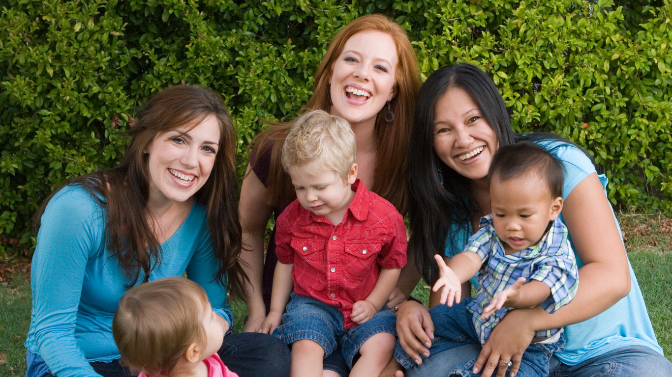 a group of women are sitting on the grass with their children .